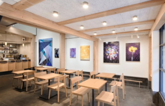 Café seating area with light wooden tables and chairs gallery walls with abstract and colorful artwork and exposed wooden beams