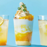 Three cold drinks on a bright blue table a lemon slice in the left glass a tall layered coffee beverage topped with whipped cream in the center and a pale drink on the right