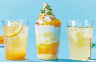 Three cold drinks on a bright blue table a lemon slice in the left glass a tall layered coffee beverage topped with whipped cream in the center and a pale drink on the right