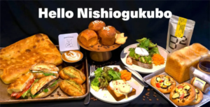 d90fc034a702b9377ed554466321acbaresized1000x510 | コーヒーステーション Bakerycafé spread featuring a large loaf sandwiches croissants savory pastries pizzas and a latte on a dark table beneath Hello Nishiogukubo text showcasing a cafe menu