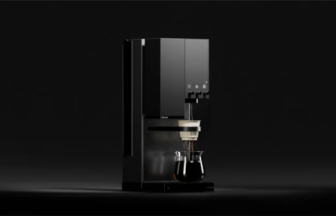 Black espresso machine with a glass carafe brewing on a dark, minimal backdrop.