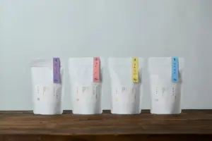 Four white stand up bags with pastel colored tabs numbered 14 arranged on a wooden surface against a pale wall product packaging