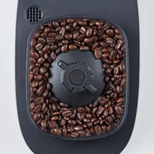 Top down view of a coffee grinder hopper filled with dark roasted beans around the central blade