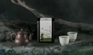 Japanese tea tin with artistic label placed between a brown teapot and two white teacups on a dark rocky backdrop