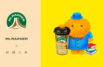 Left side shows the Mt RAINIER logo and Japanese text right side features an orange plush figure wearing a blue coat and hat holding a Mt RAINIER coffee cup and books on a bright yellow background