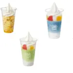 Six clear dessert cups with swirled whipped cream on top in colors including orange red blue green and mango scattered on a white background