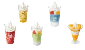 Six clear dessert cups with swirled whipped cream on top in colors including orange red blue green and mango scattered on a white background