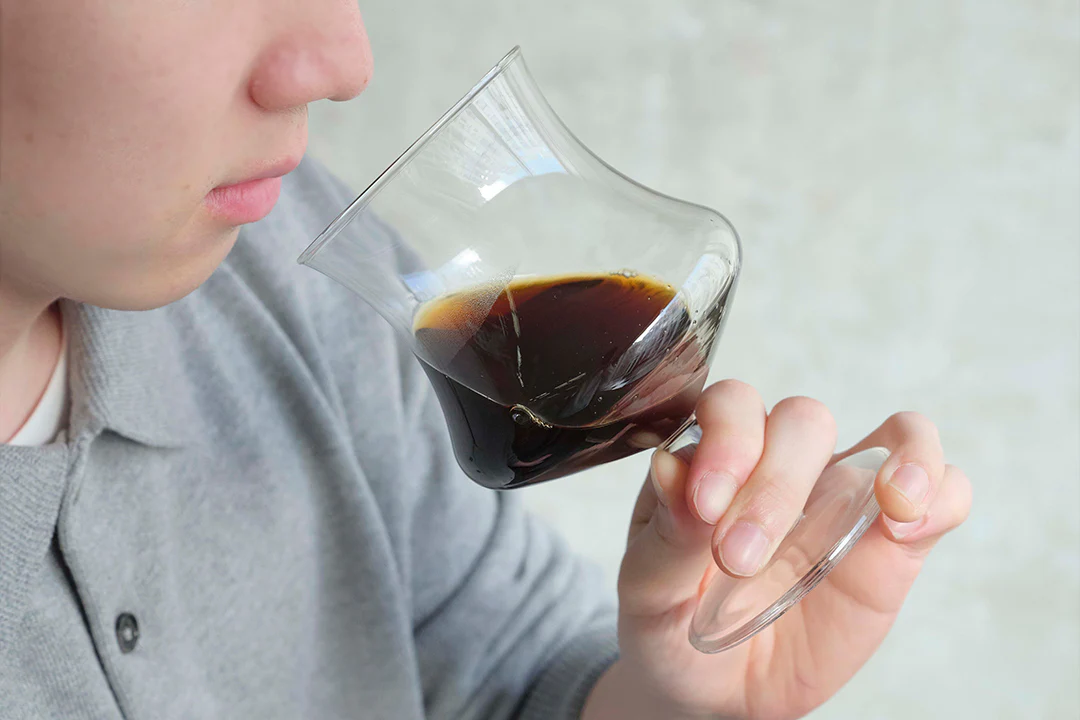 Close up of a person sipping dark coffee from a curved stemmed glass