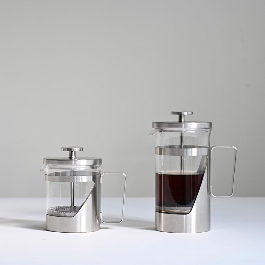 Two French press coffee makers small and large with metal and glass bodies on a white surface
