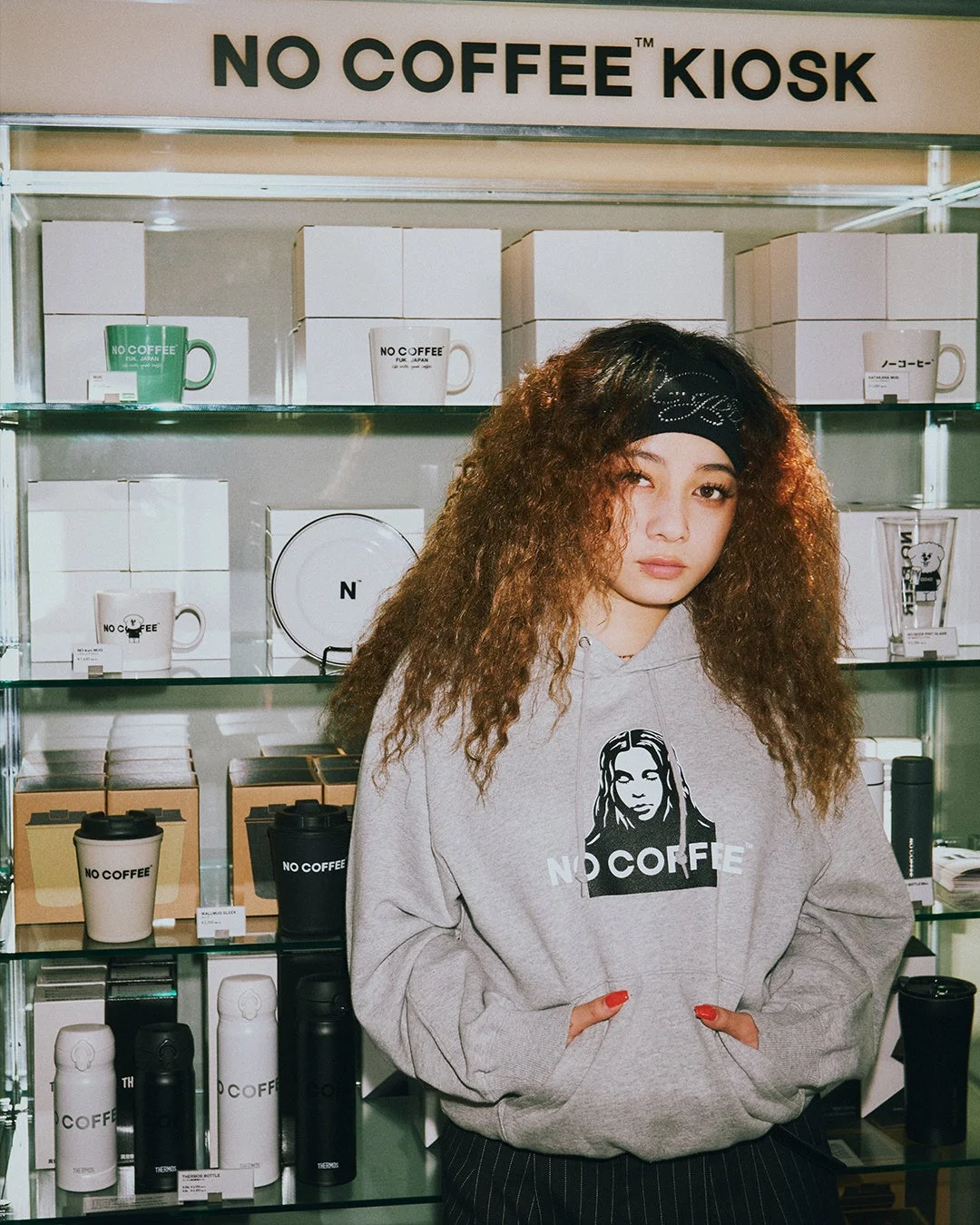NO COFFEE KIOSKのディスプレイとロゴ入りパーカーを着用した女性