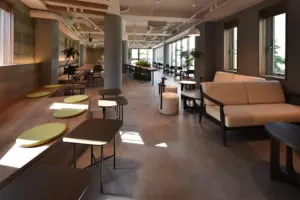 Modern open plan lounge with long wooden table round stools and green cushions along a bench seating area by windows