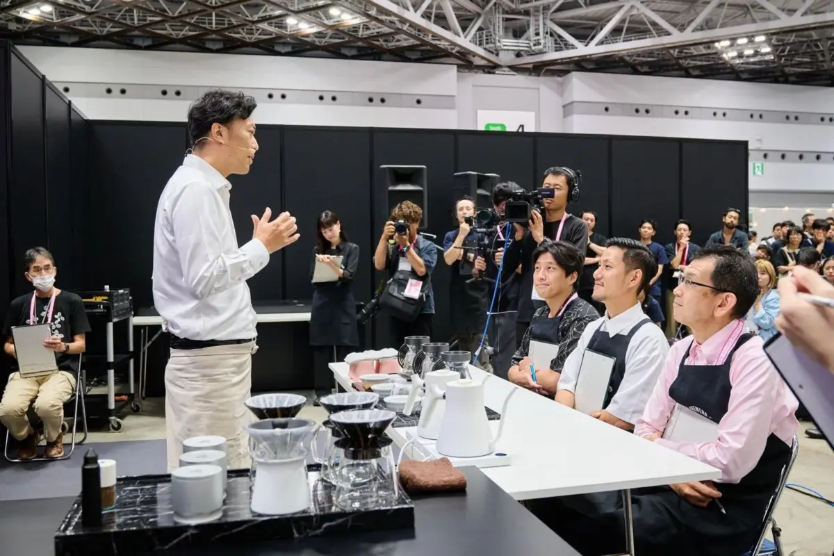 広々とした会場で、バリスタらしき男性がコーヒーの淹れ方についてデモンストレーションを行っています。