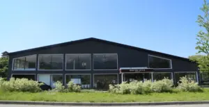 Two story dark building housing Maruyama Coffee with large glass storefront windows and shrubs in front