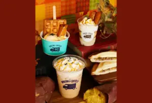Assorted dessert drinks and snacks a topped cup with waffles a caramel whipped cream drink and a sandwich on a wooden board cozy autumn setup
