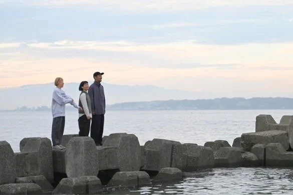 海を背景に防波堤に立つ三人の人物