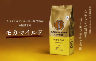 Package of Sarutahiko Coffee Mocha Mild (150g) with gold and yellow design, logo on front, against a warm brown background; Japanese branding text on left and vertical slogan on right.
