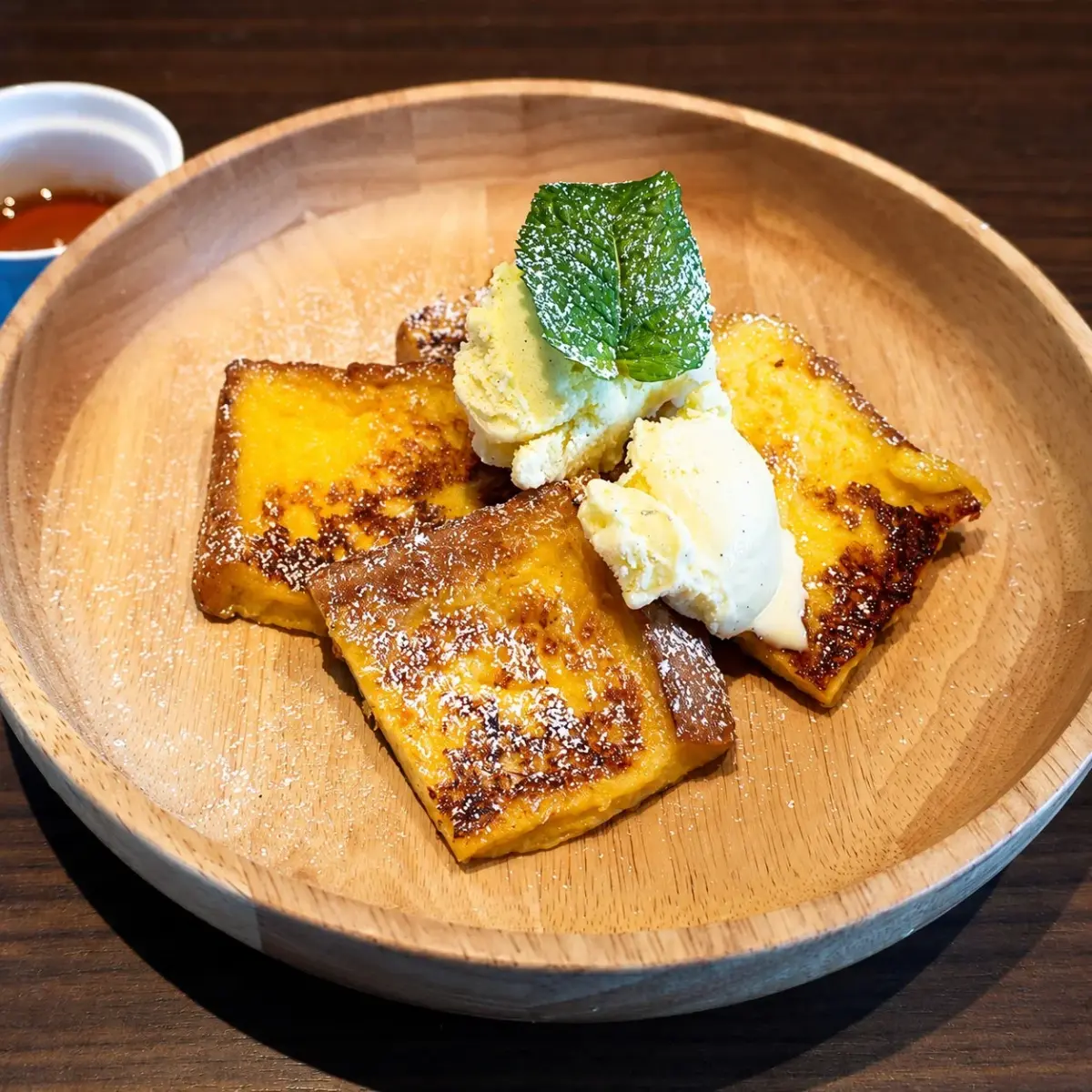 焼き色のついたフレンチトーストが木製の皿に盛り付けられ、バニラアイスとミントの葉が添えられている画像