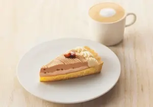 Slice of chocolate cream tart on a white plate with a cup of coffee in the background