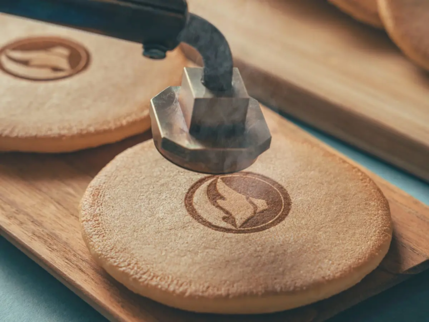 Close up of a metal stamp pressing into a round wooden disc with a circular flame logo being imprinted