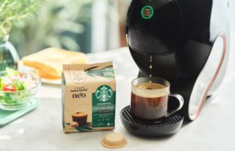 Espresso machine dispensing coffee into a cup on a saucer with a Starbucks Dolce Gusto Neo roast box and a coffee capsule on the counter nearby