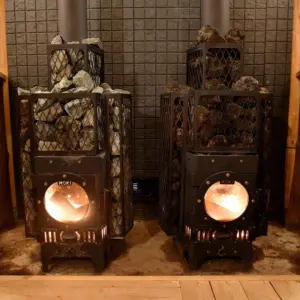 Two black wood burning stoves with rock filled cages glowing flames in a tiled room