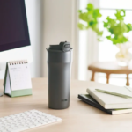 Grey Thermos on a wooden desk with notebooks a calendar and a computer monitor in a bright tidy workspace