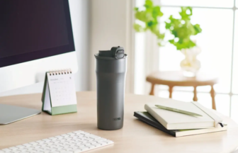 Grey Thermos on a wooden desk with notebooks a calendar and a computer monitor in a bright tidy workspace
