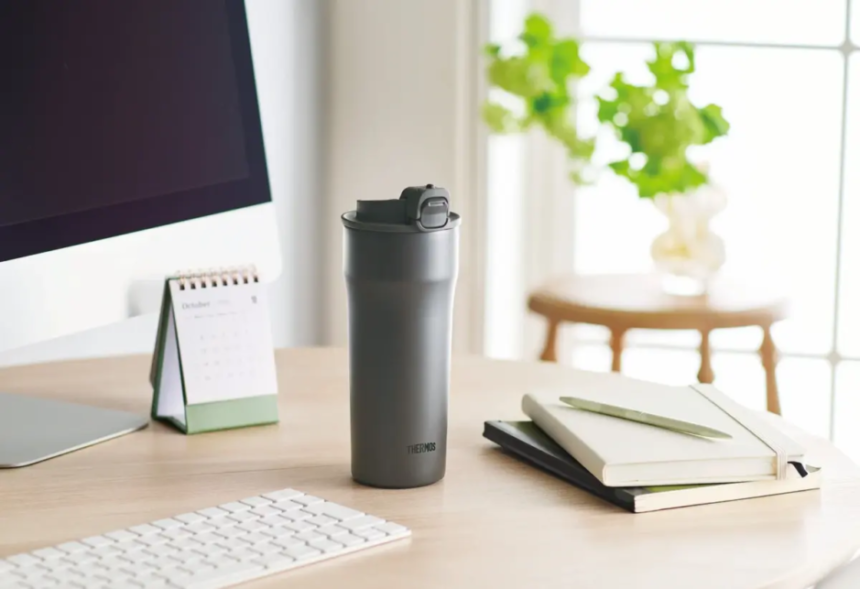 Grey Thermos on a wooden desk with notebooks a calendar and a computer monitor in a bright tidy workspace