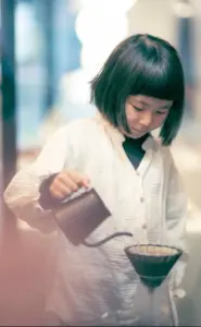 47103d390333adc2fdf6585da58dd99d | コーヒーステーション Young girl with short black hair pouring water from a kettle into a pour over coffee dripper