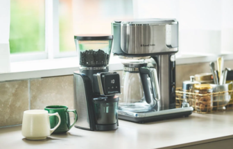 Stainless steel espresso machine and coffee grinder on a kitchen counter with two mugs nearby.