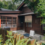 Wooden cafe building with a striped awning and Japanese signage nestled among lush greenery outside the entrance