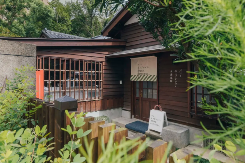 Wooden cafe building with a striped awning and Japanese signage nestled among lush greenery outside the entrance