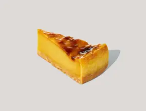 Slice of lemon tart with a glossy caramelized top and a crumb crust on a light background