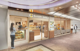 Bakery cafe storefront with glass display case of pastries and customers ordering inside a modern mall corridor