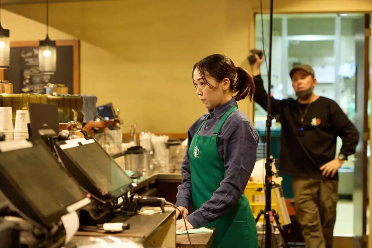 スターバックスのようなカフェのカウンターで、緑のエプロンをつけた女性が作業している