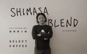 Man with arms crossed posing in front of a wall branded with SHIMASA BLEND and SELECT COFFEE