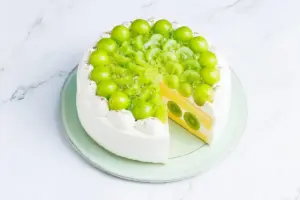 White frosted cake topped with a circle of green grapes cross section shows kiwi slices between yellow cake layers