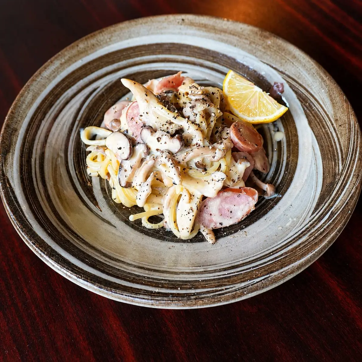 渦巻き模様の皿に盛られた、きのこやベーコンが入ったクリーミーなパスタ