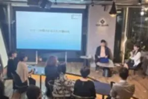 Panel discussion in a modern room with two speakers onstage a projected presentation screen and an attentive audience seated at tables