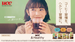 Woman smiles while holding a cup of coffee in a green themed UCC advertisement with product packs at the bottom