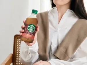 Person holding a Starbucks Coffee of the Day bottle with a green cap displayed against a light background