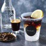 Iced beverage in a clear cup with a lime wedge and a MACHI cafe+ logo on a dark bar counter