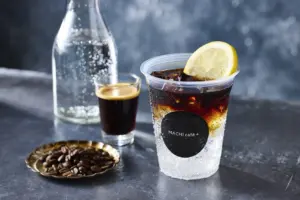 Iced beverage in a clear cup with a lime wedge and a MACHI cafe+ logo on a dark bar counter