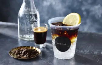 Iced beverage in a clear cup with a lime wedge and a MACHI cafe+ logo on a dark bar counter