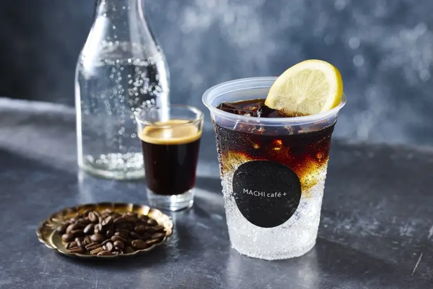 Iced beverage in a clear cup with a lime wedge and a MACHI cafe+ logo on a dark bar counter