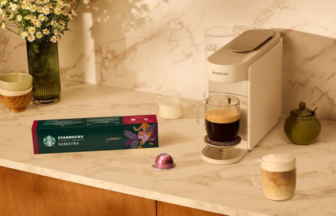 Marble kitchen counter with a Nespresso machine a glass mug of coffee a Starbucks Sumatra box and a pink coffee capsule beside a vase of daisies