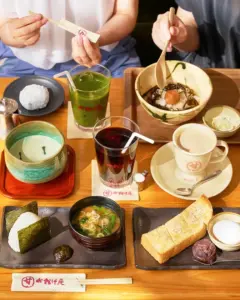 Japanese meal spread with onigiri miso soup tamagoyaki pickles and tea on a wooden table multiple bowls and drinks add variety to the scene