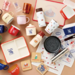 Assorted Komedas Coffee mugs cups containers and kitchenware arranged on a beige surface showcasing branded tableware set