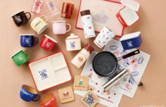 Assorted Komedas Coffee mugs cups containers and kitchenware arranged on a beige surface showcasing branded tableware set