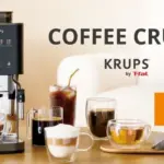 Krups Coffee Crush espresso machine on a wooden table with cups and a carafe orange tag with Japanese text on the right